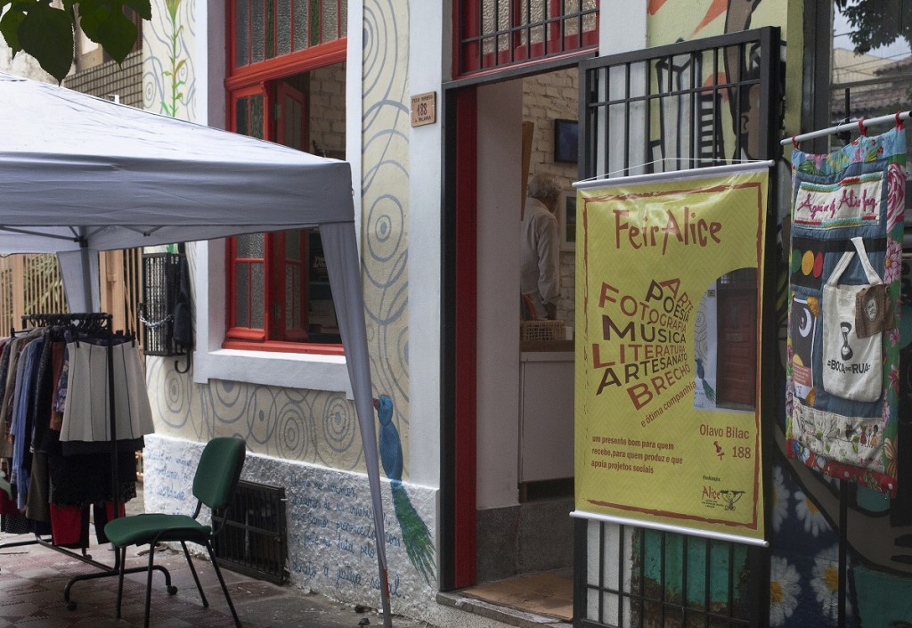 Fachada da Casa Alice, mostrando uma edição da FeirAlice. Algumas roupas em uma arara são  e banner da FeiraAlice são expostos na calçada.